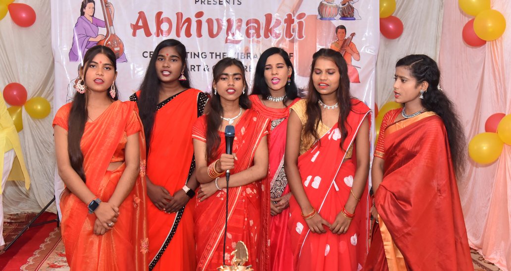 Female students singing group song wearing red sarees